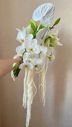 a bouquet of white flowers is held up by someone's hand in front of a wall