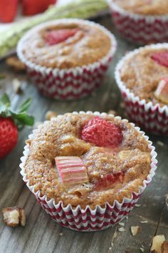 several muffins with strawberries on the side sitting on a wooden table next to some leaves