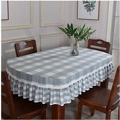 a dining room table with a checkered tablecloth and vase filled with green plants