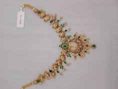 a gold necklace with green and white stones on it, along with a price tag