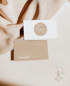 two business cards sitting on top of a white cloth covered tablecloth with a logo