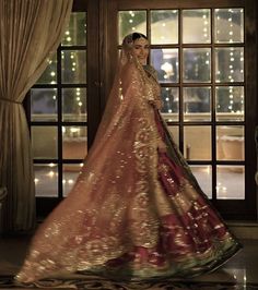 a woman in a red and gold lehenga is standing by a window with lights