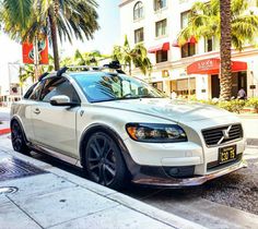 a white volvo car parked on the side of the road in front of palm trees