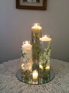 candles are lit on a table with flowers and greenery in glass vases, along with lace doily