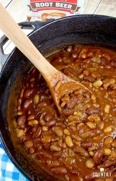 a wooden spoon in a pot filled with chili and beans on top of a blue checkered table cloth