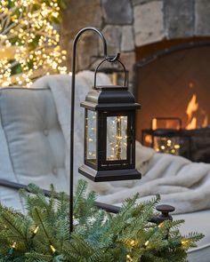 a lit lantern sitting on top of a table next to a christmas tree in front of a fireplace