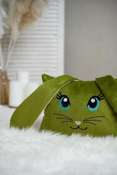 a green cat purse sitting on top of a white fur covered floor next to a window