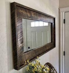 a mirror hanging on the side of a wall next to a vase with flowers in it