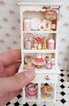 a hand holding a doll house in the middle of a room with black and white flooring