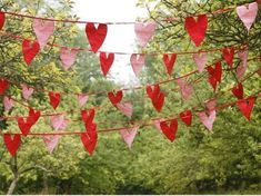 red and pink hearts are hanging from a line in the woods with trees behind them