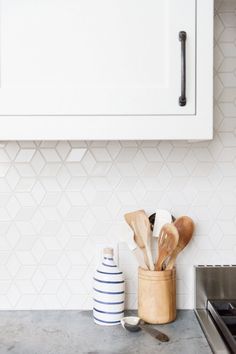 kitchen utensils in wooden holder on counter top next to stove with white tile backsplash