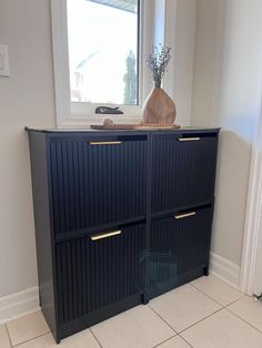 a black cabinet with gold handles in a room next to a white wall and window