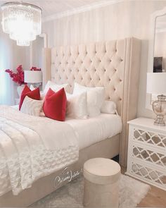 a bedroom with white furniture and red pillows on the headboard, along with a chandelier