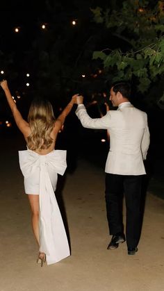 a man and woman walking down a path at night with their arms in the air