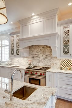 a kitchen with white cabinets and marble counter tops, an oven and sink in the center