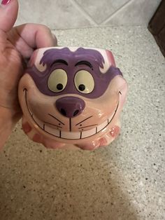 a hand holding a purple and white ceramic cat toy with eyes on it's face