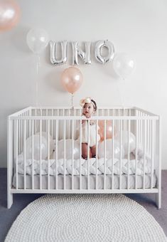 a baby in a white crib with balloons and the word uno spelled above it