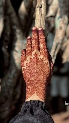 a woman's hand with henna tattoos on it holding a stick in front of some trees