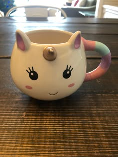 a ceramic mug with a cat face on it's side sitting on a wooden table