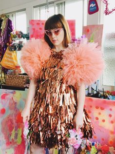 a woman standing in front of a painting with pink and gold feathers on her shoulders