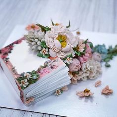 an open book sitting on top of a white table next to flowers and paper petals