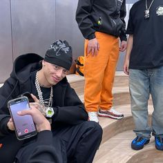 a man sitting on the steps with his cell phone in his hand and two other men standing behind him