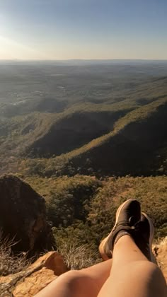 someone's feet resting on the edge of a cliff overlooking a valley and mountains