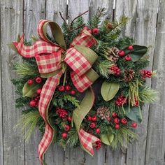 a christmas wreath hanging on the side of a wooden fence with red berries and pine cones