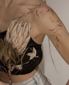 a woman wearing a crop top with feathers on her shoulder and arm, holding a plant