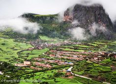 an aerial view of a lush green valley with houses and mountains in the back ground