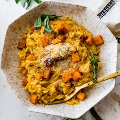 a white bowl filled with pasta covered in parmesan cheese and topped with fresh herbs