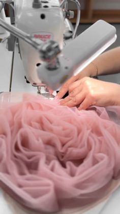 a woman is using a sewing machine to sew pink fabric on a white table