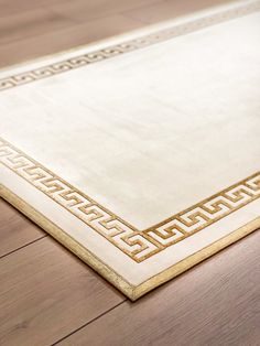 a white rug with gold border on top of a wooden floor in an empty room