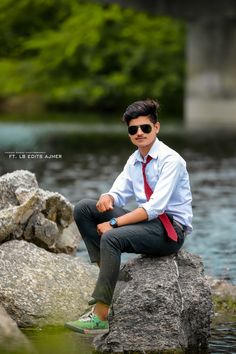 a man sitting on top of a rock next to a river wearing sunglasses and a tie