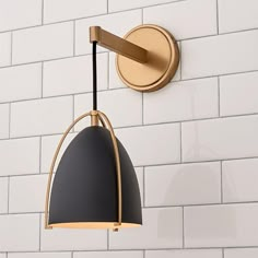 a black and gold light hanging from the side of a white brick wall in a bathroom