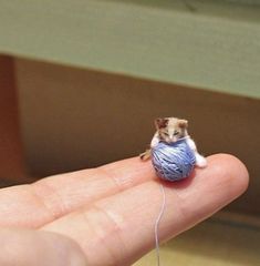 a tiny mouse sitting on top of a blue ball of yarn in someone's hand