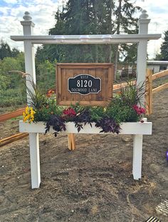 a wooden sign with flowers and plants on it in front of a fenced area