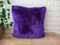 a purple pillow sitting on top of a wooden table next to a potted plant