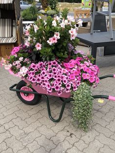 a wheelbarrow filled with pink and white flowers on top of a stone ground