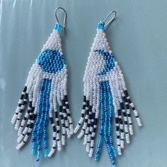 two blue and white beaded earrings on a gray surface with one dangling from the back