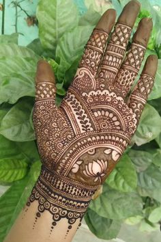 the hand is decorated with henna on it and green leaves in the back ground