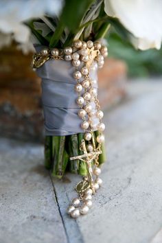 a bridal bouquet with white flowers and pearls on the end is wrapped in gray satin