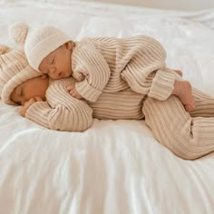 a baby laying on top of a white bed next to a teddy bear wearing a hat