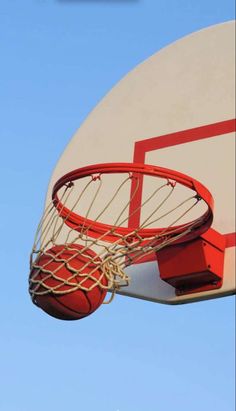 a basketball going through the rim of a basketball hoop with blue sky in the background