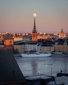 the moon is setting over a city with tall buildings and a large boat in the water