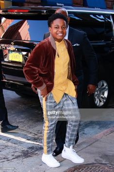 a young man in plaid pants and a yellow shirt is standing on the sidewalk