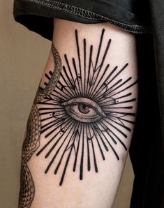 an all seeing eye tattoo on the left leg with black lines and snakes around it