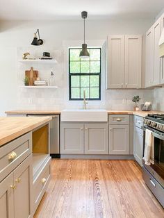 a kitchen with white cabinets and wood floors, an oven, sink, dishwasher and window