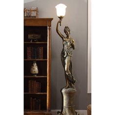 a bronze statue holding a lamp next to a book shelf