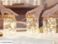 three jars with fairy lights in them are being held by two hands over a table